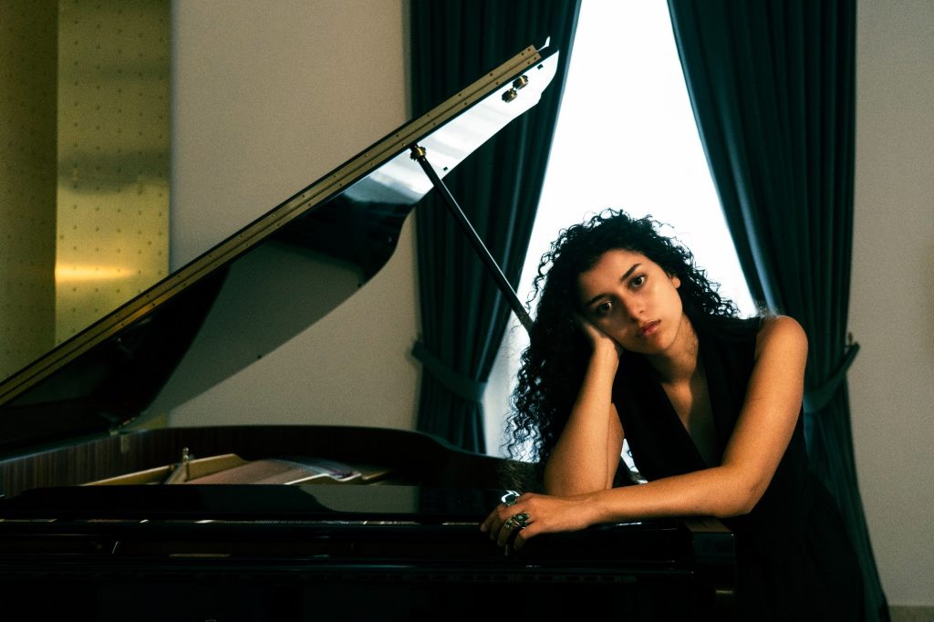 Carlotta Maestrini appoggiata al pianoforte a coda, davanti a una tenda scura